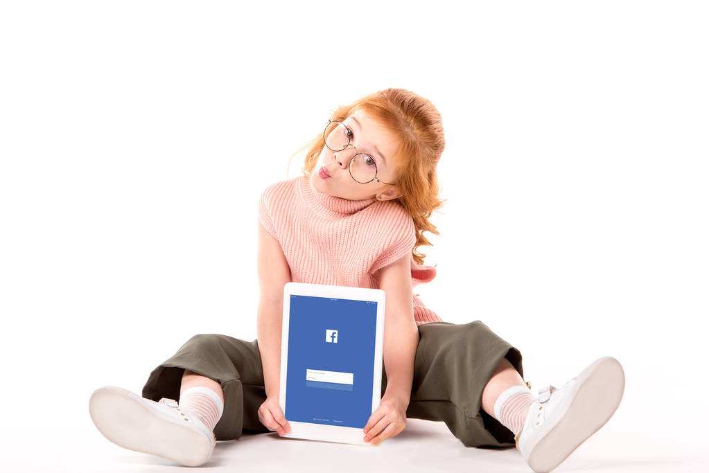 niño de pelo rojo sentado y sosteniendo la tableta con la página de Facebook cargada en blanco
 - Foto, imagen