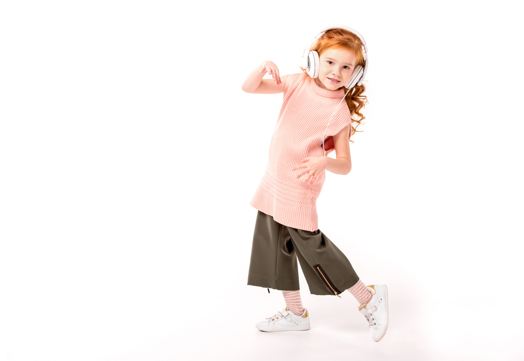 criança cabelo vermelho em fones de ouvido dançando e olhando para a câmera no branco
 - Foto, Imagem