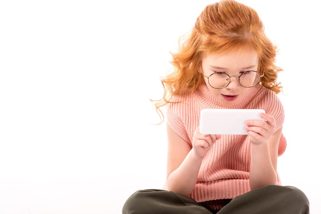 smartphone üzerinde beyaz izole bakarak sürpriz Kızıl saçlı çocuk - Fotoğraf, Görsel
