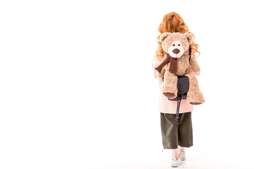 rear view of red hair kid standing with teddy bear on back isolated on white - Photo, Image