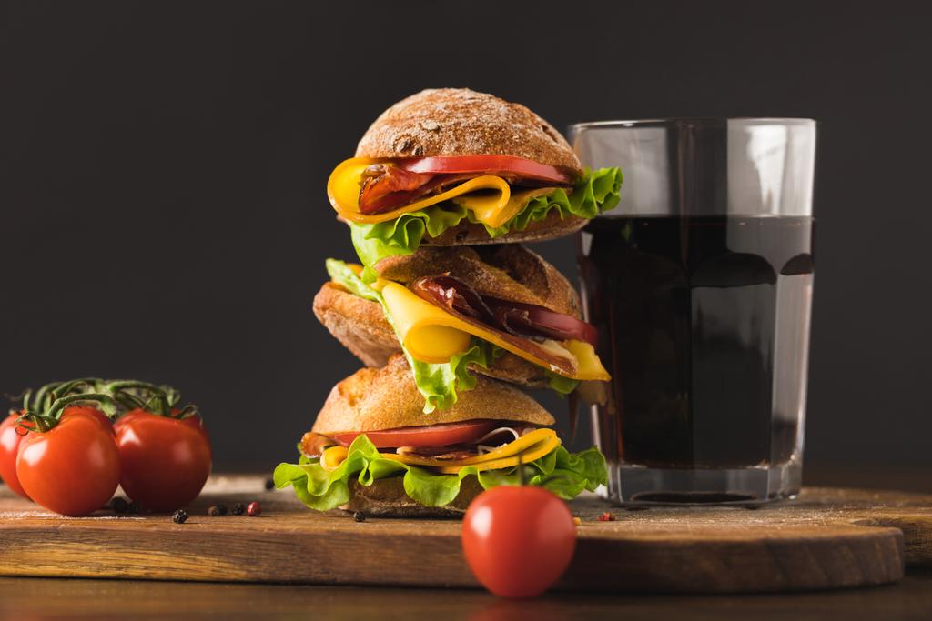 grote sandwich met cherry tomaten en een glas cola op de snijplank - Foto, afbeelding