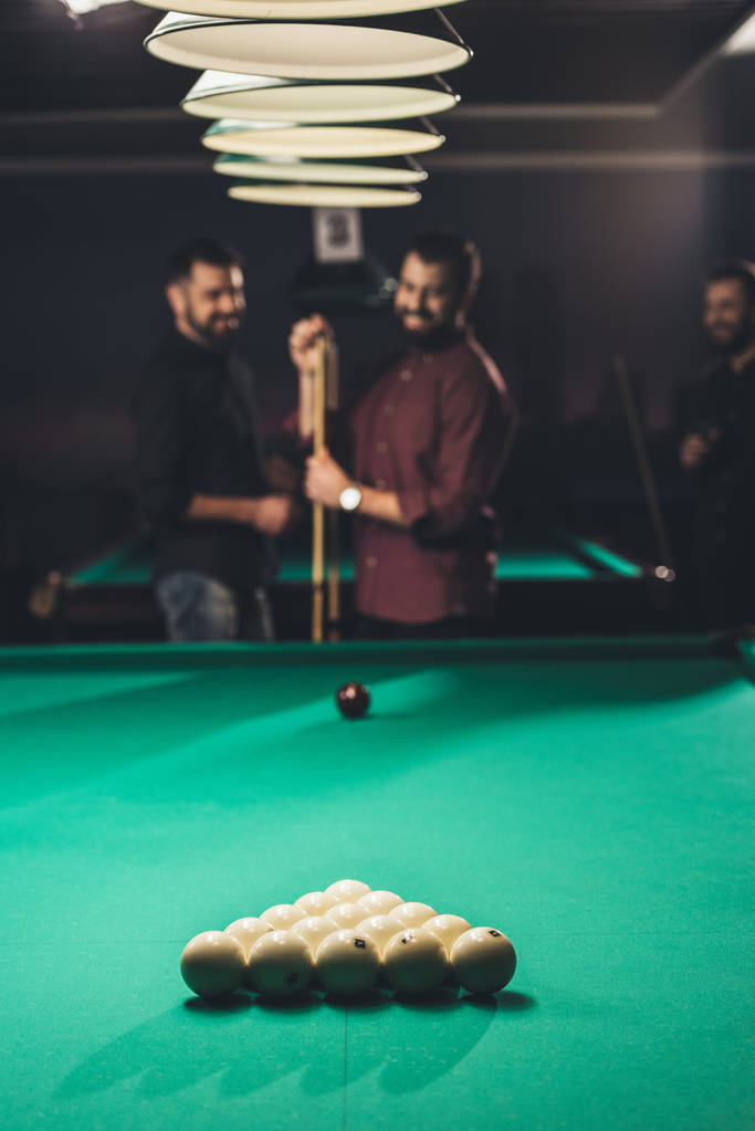 smiling man rubbing cue with chalk beside pool table at bar with friends - Photo, Image