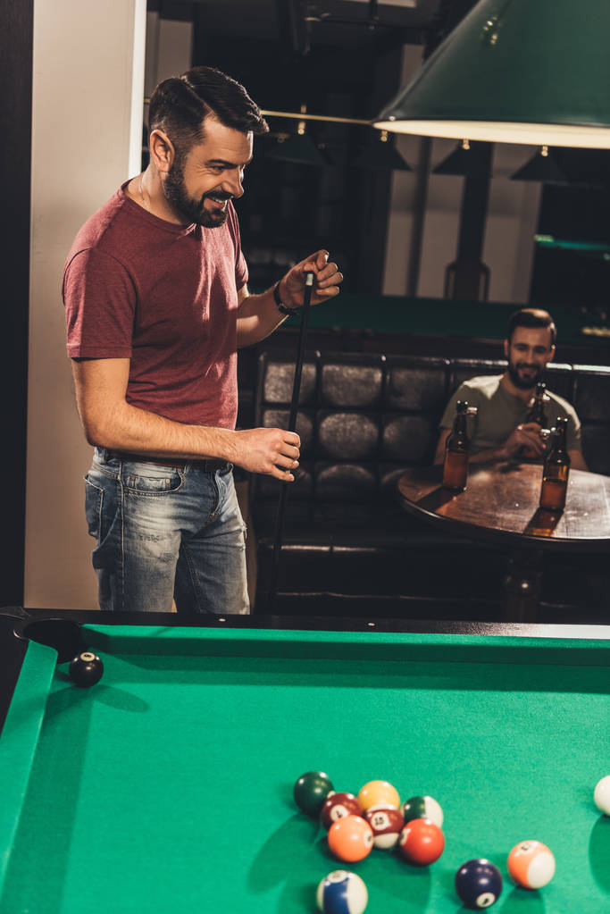 cheerful caucasian man chalking billiard cue at bar with friend - Photo, Image