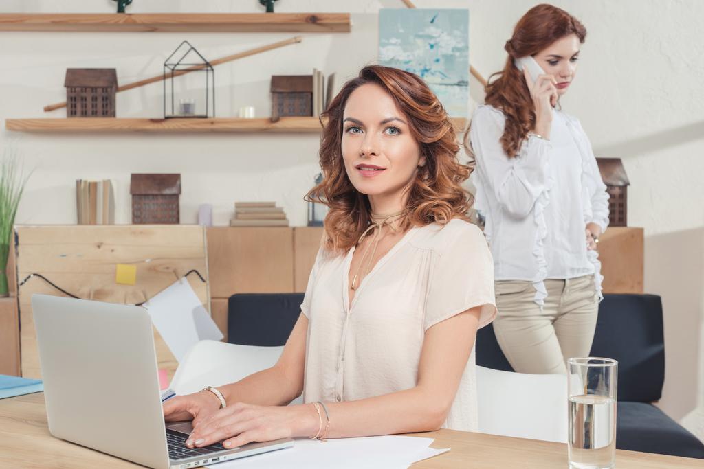 jovem empresária trabalhando com laptop no escritório, enquanto seu colega falando por telefone
 - Foto, Imagem