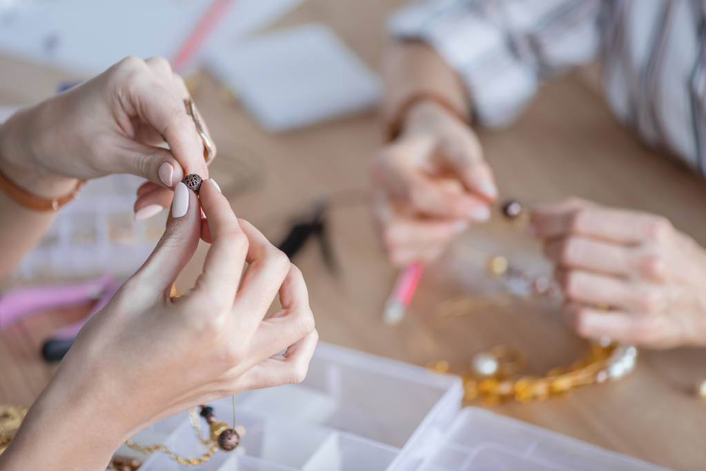 abgeschnittene Aufnahme von Frauen, die in einer Werkstatt Zubehör aus Perlen herstellen - Foto, Bild