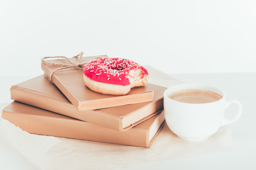 delicious pink doughnut on stacked books with cup of coffee - Photo, Image