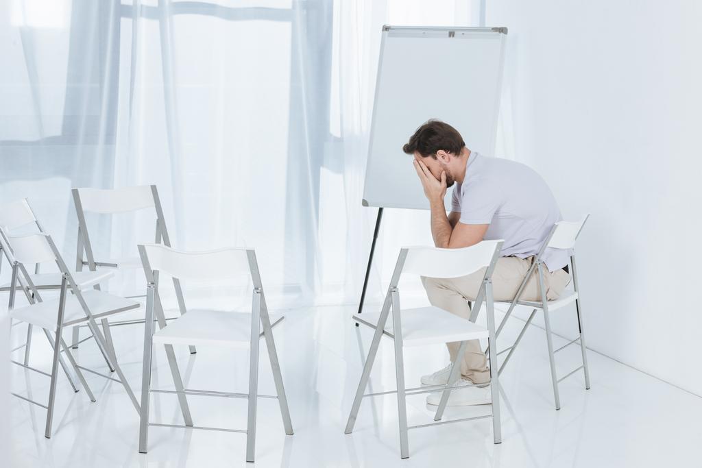 depresivní středního věku muž sedí na židli v prázdné místnosti - Fotografie, Obrázek