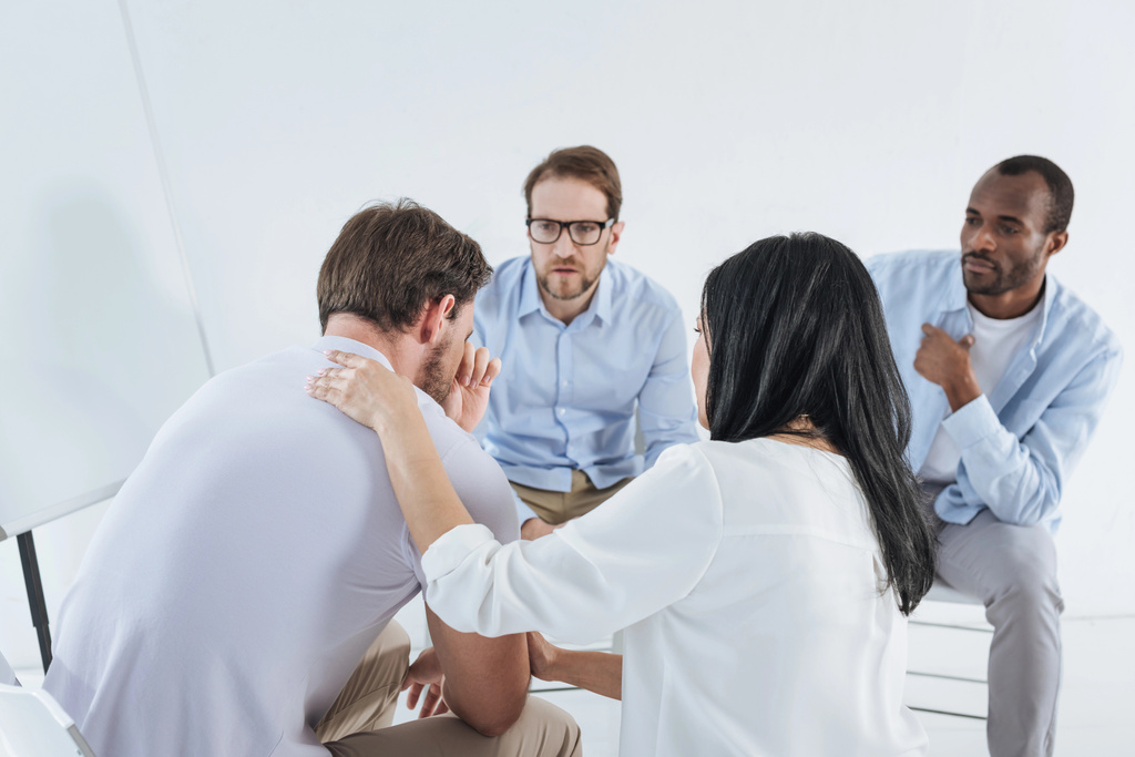 multiethnic mid adult people sitting on chairs and supporting upset man during anonymous group therapy    - Photo, Image