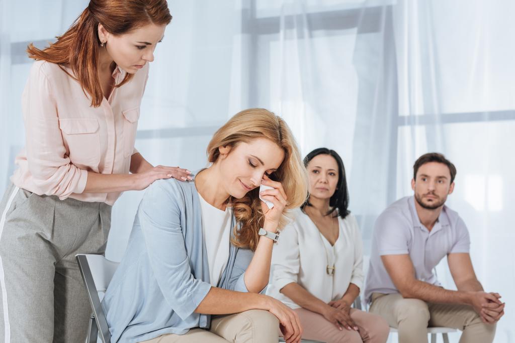 keski-ikäiset ihmiset tukevat itkevää naista nimettömän ryhmähoidon aikana
 - Valokuva, kuva