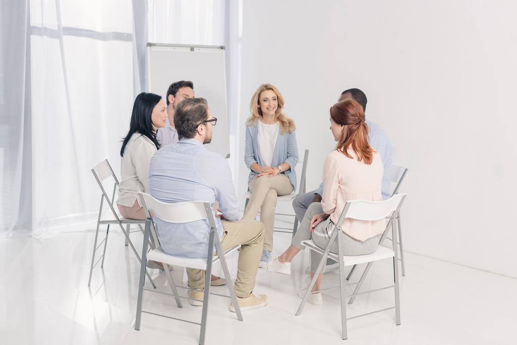 multi-etnisch midden leeftijd mensen zitten op stoelen en te praten tijdens groepstherapie - Foto, afbeelding