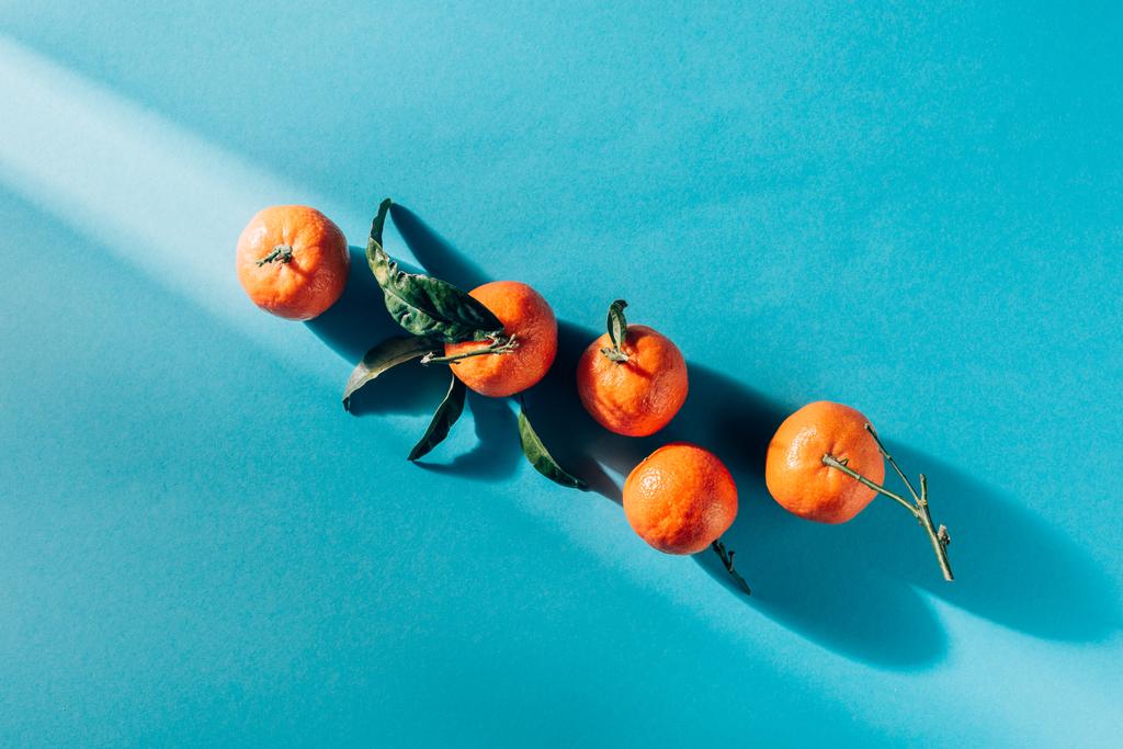 top view of arranged tangerines with leaves on blue surface - Photo, Image