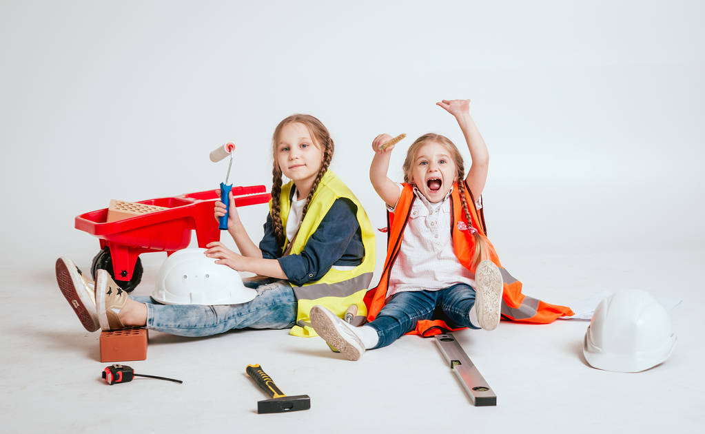 Twee kleine vrolijke meisjes met vlechten spelen in reparatie of bouw op wit - Foto, afbeelding