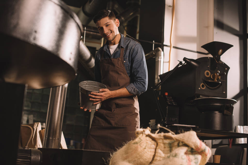 young coffee roaster with metal bucket in hands working in coffee shop - Photo, Image