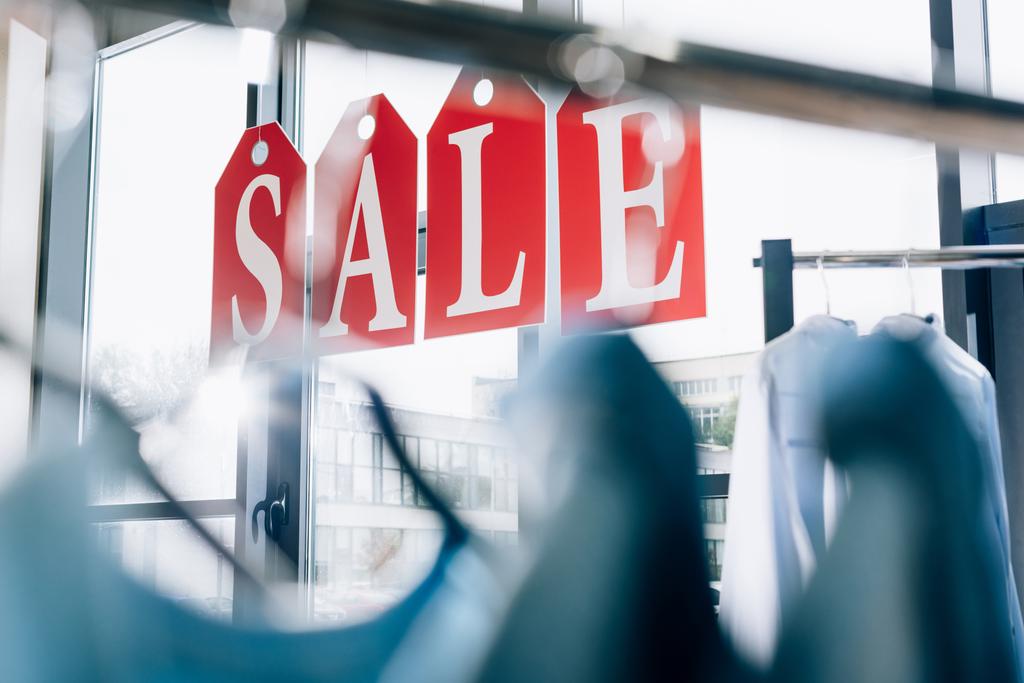 знак продажи из тегов с буквами на окнах бутика с вешалками на переднем плане
 - Фото, изображение