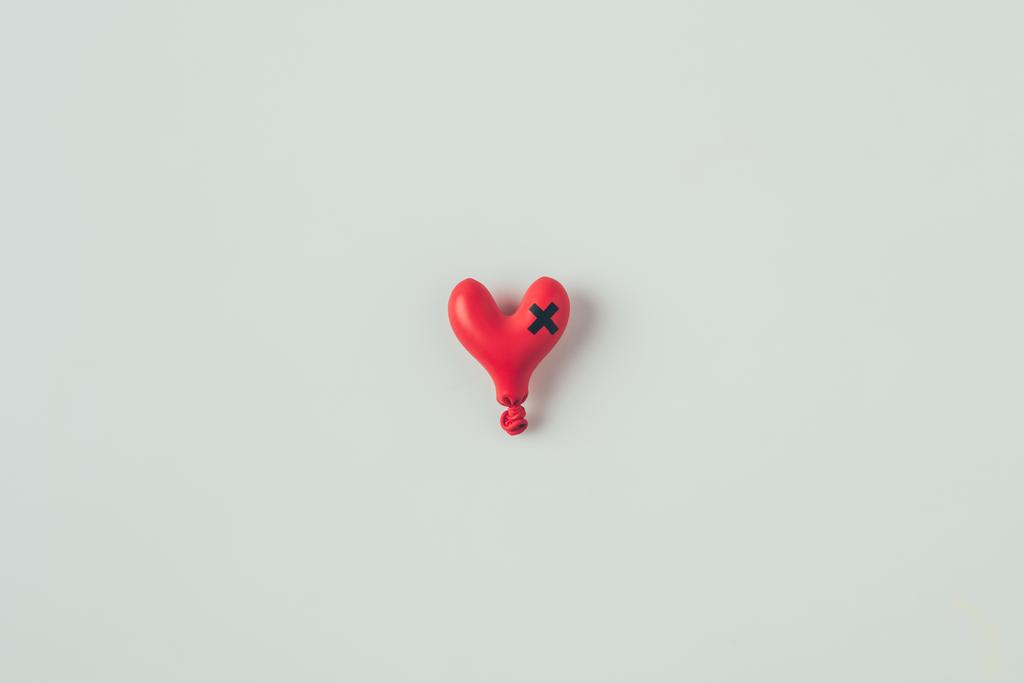 bovenaanzicht van gededegeerde hartvormige ballon met isolerende tape cross geïsoleerd op wit, Valentines Day concept - Foto, afbeelding