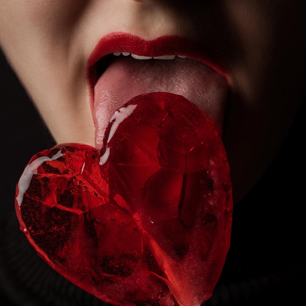 immagine ritagliata di donna leccare lecca-lecca a forma di cuore isolato su nero, concetto di giorno di San Valentino
 - Foto, immagini