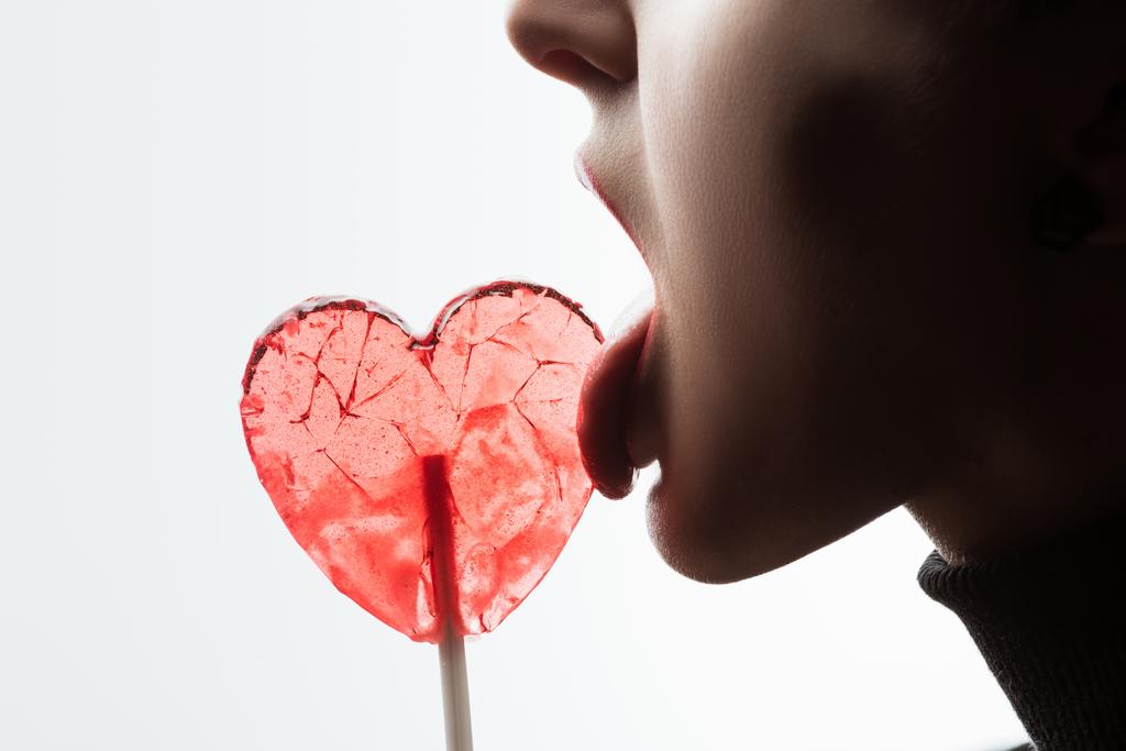 bijgesneden beeld van vrouw likken hartvormige Lollipop geïsoleerd op wit, Valentines Day concept - Foto, afbeelding