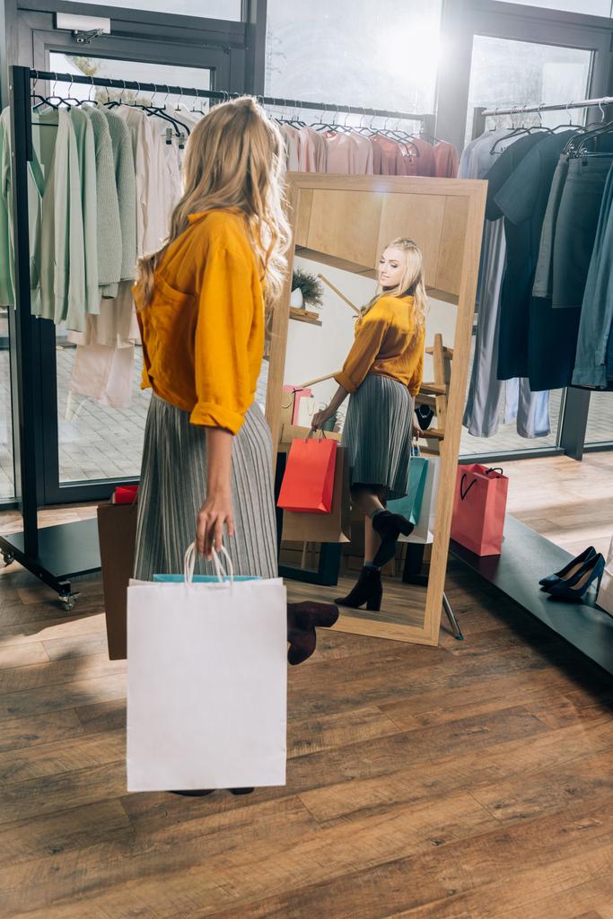 beautiful young woman looking at mirror in clothing store - Photo, Image