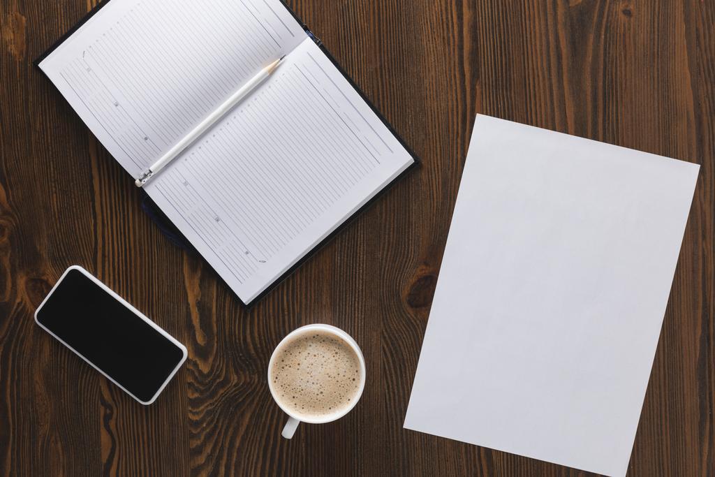 flache Liege mit Smartphone, Notizbuch, Bleistift und Kaffeetasse auf Holztischplatte - Foto, Bild