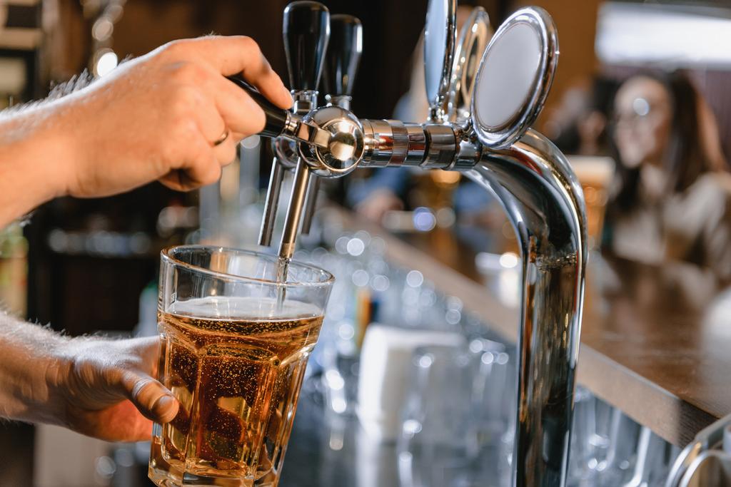 обрезанное изображение бармена, наливающего пиво в стекло в баре
 - Фото, изображение