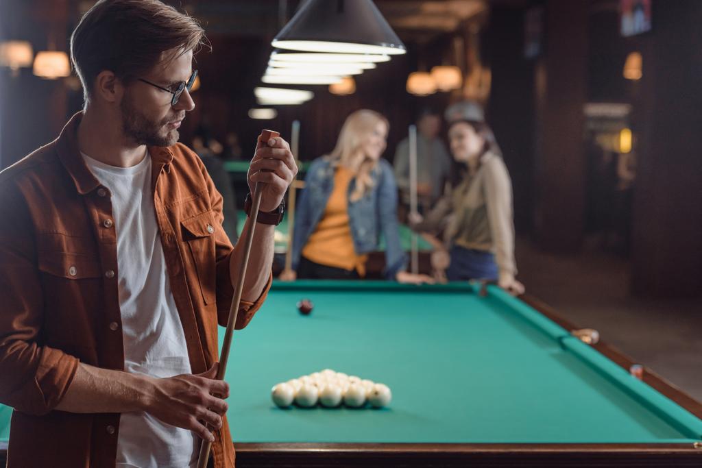 young man chalking cue beside pool table at bar with friends  - Photo, Image