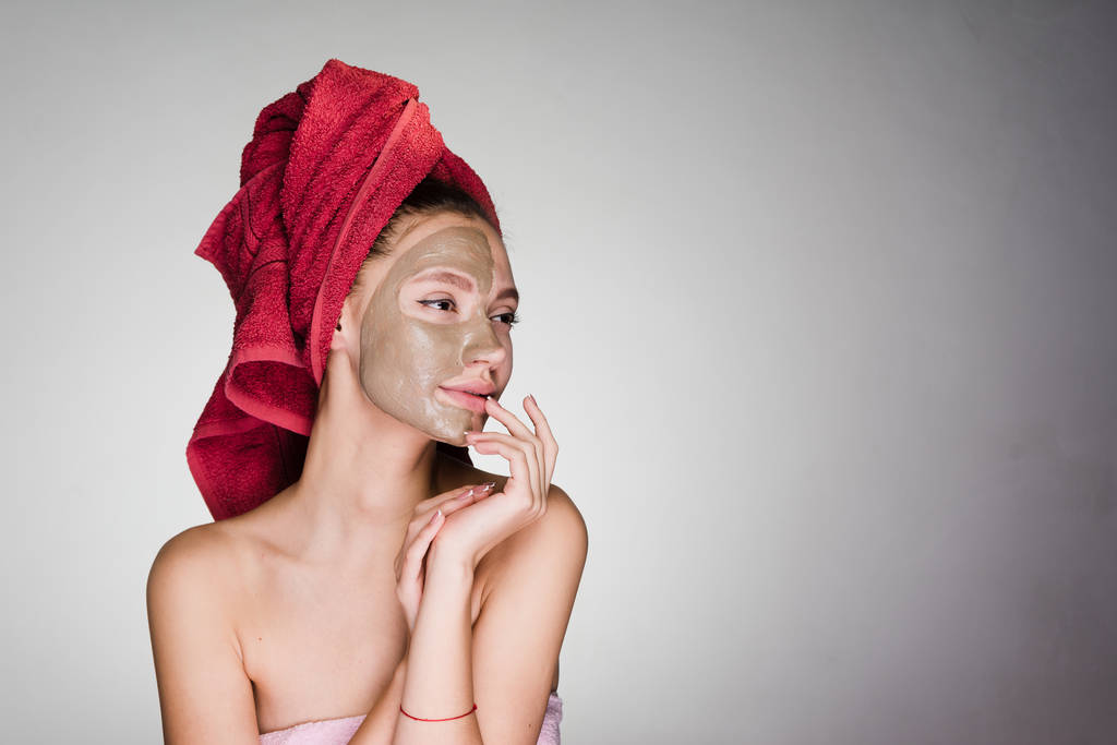 krásná dívka se stará o sama, lázeňské procedury, jílová maska na obličeji, na hlavě červený ručník - Fotografie, Obrázek