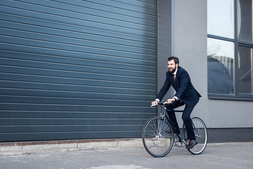 Caddede bisiklet sürme takım elbiseli genç işadamı gülümseyen - Fotoğraf, Görsel