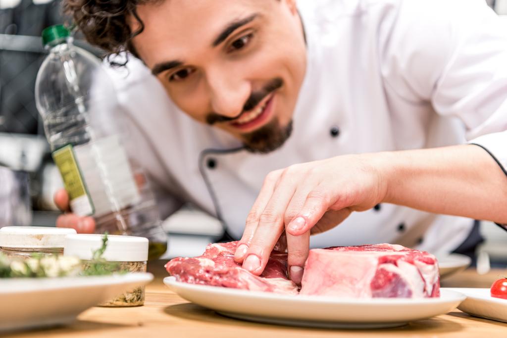 Chef sorrindo adicionando óleo à carne crua
 - Foto, Imagem