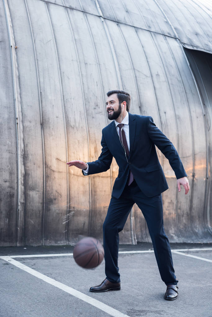 boční pohled veselý podnikatel v sluchátka hrát basketbal na ulici - Fotografie, Obrázek