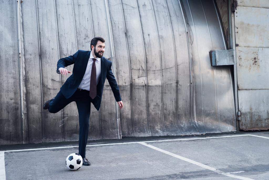 νεαρός χαμογελαστό επιχειρηματίας στο κοστούμι παίζοντας ποδόσφαιρο στην οδό - Φωτογραφία, εικόνα