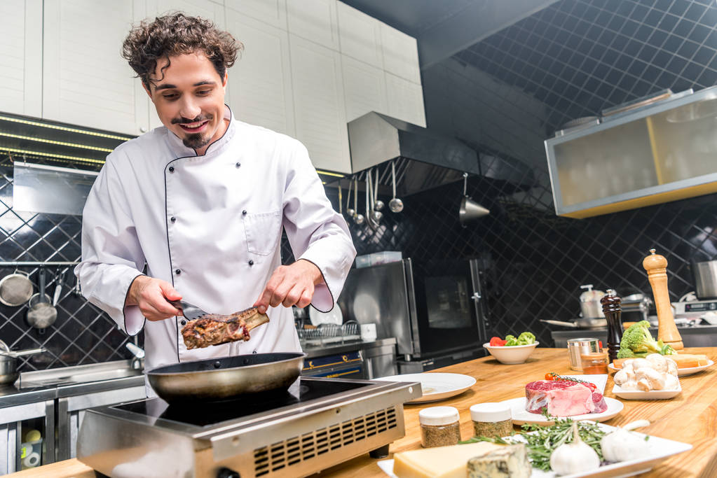 Chef sorrindo fritar carne na cozinha do restaurante
 - Foto, Imagem