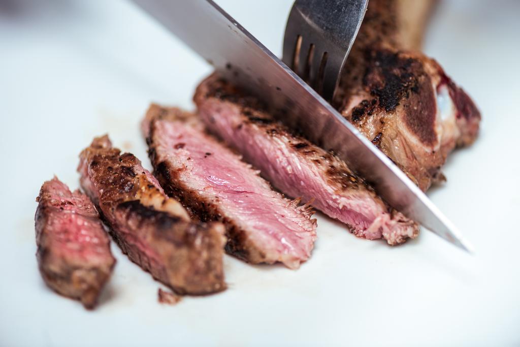 περικομμένη εικόνα του chef κοπή τηγανητό κρέας με μαχαίρι και πιρούνι - Φωτογραφία, εικόνα