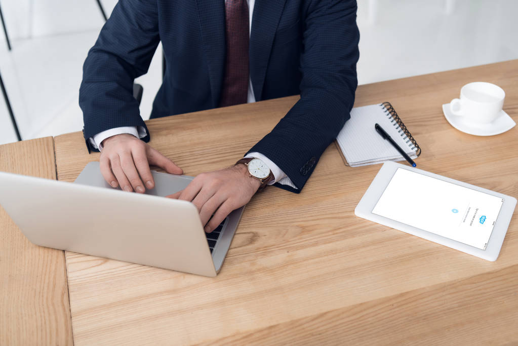vista parcial del empresario que trabaja en el ordenador portátil en el lugar de trabajo con la tableta en la oficina
 - Foto, imagen