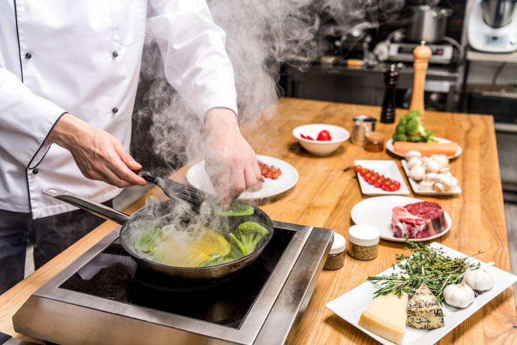 immagine ritagliata dello chef che frigge peperoni gialli e verdi con broccoli
 - Foto, immagini