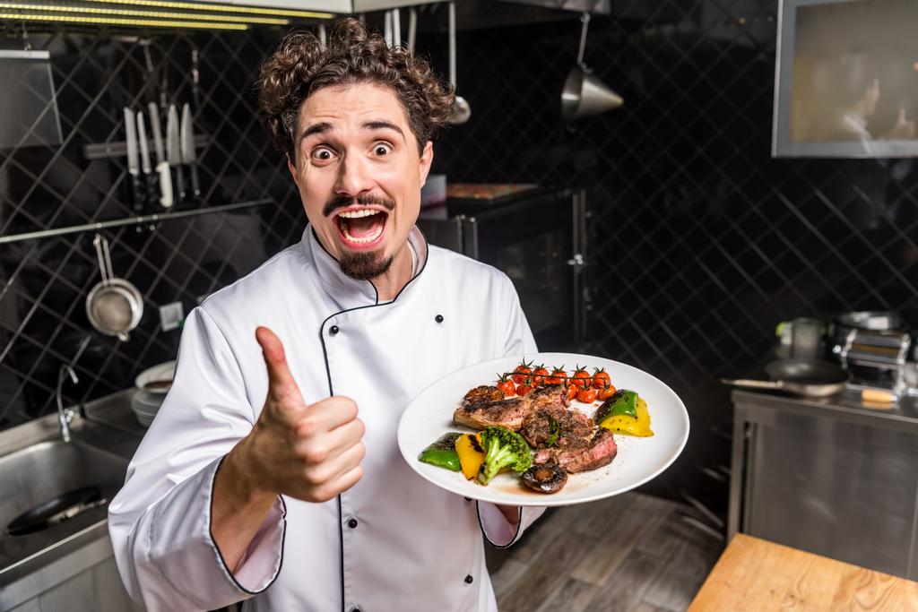 Chef sonriente gritando mostrando el pulgar hacia arriba y sosteniendo verduras cocidas con carne
  - Foto, imagen