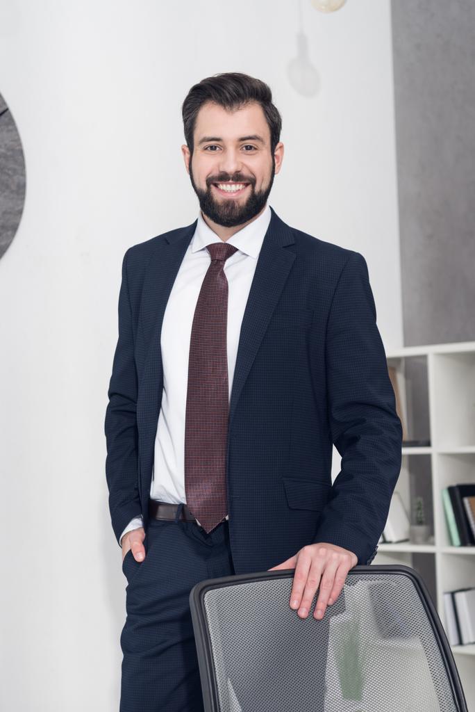 portrait of cheerful businessman in suit standing at workplace in office - Photo, Image