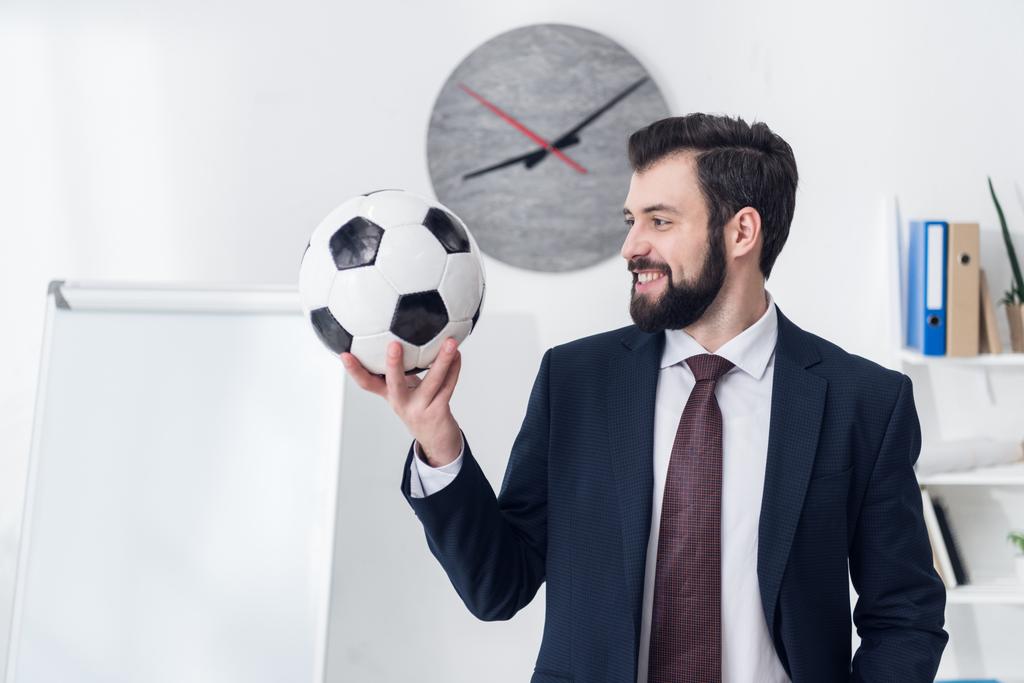 πορτρέτο του χαμογελώντας επιχειρηματίας κρατώντας την μπάλα ποδοσφαίρου στο γραφείο - Φωτογραφία, εικόνα
