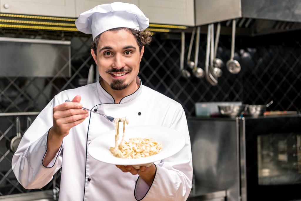 chef souriant tenant assiette avec pâtes et fourchette dans les mains
 - Photo, image