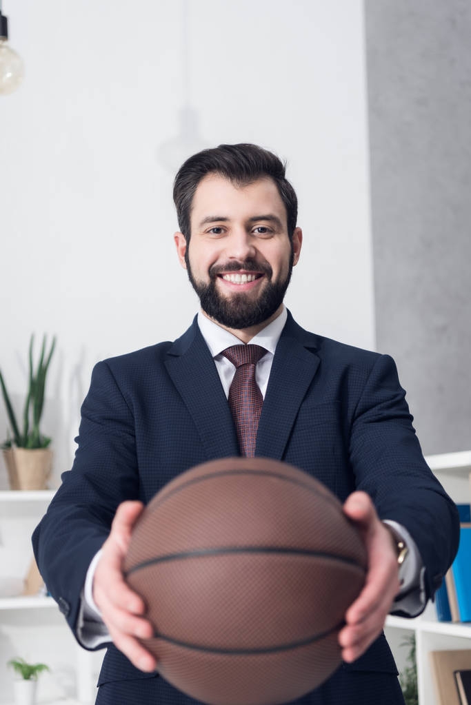 избирательный фокус улыбающегося бизнесмена, показывающего баскетбольный мяч в руках в офисе
 - Фото, изображение
