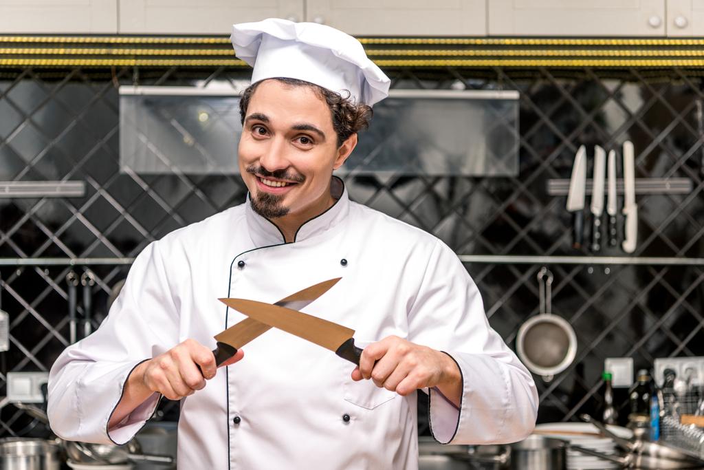 lachende chef-kok permanent met gekruiste messen - Foto, afbeelding