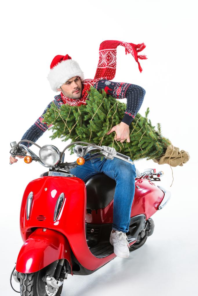 homem em santa chapéu e cachecol segurando árvore de Natal enquanto montando scooter vermelho, isolado em branco
 - Foto, Imagem