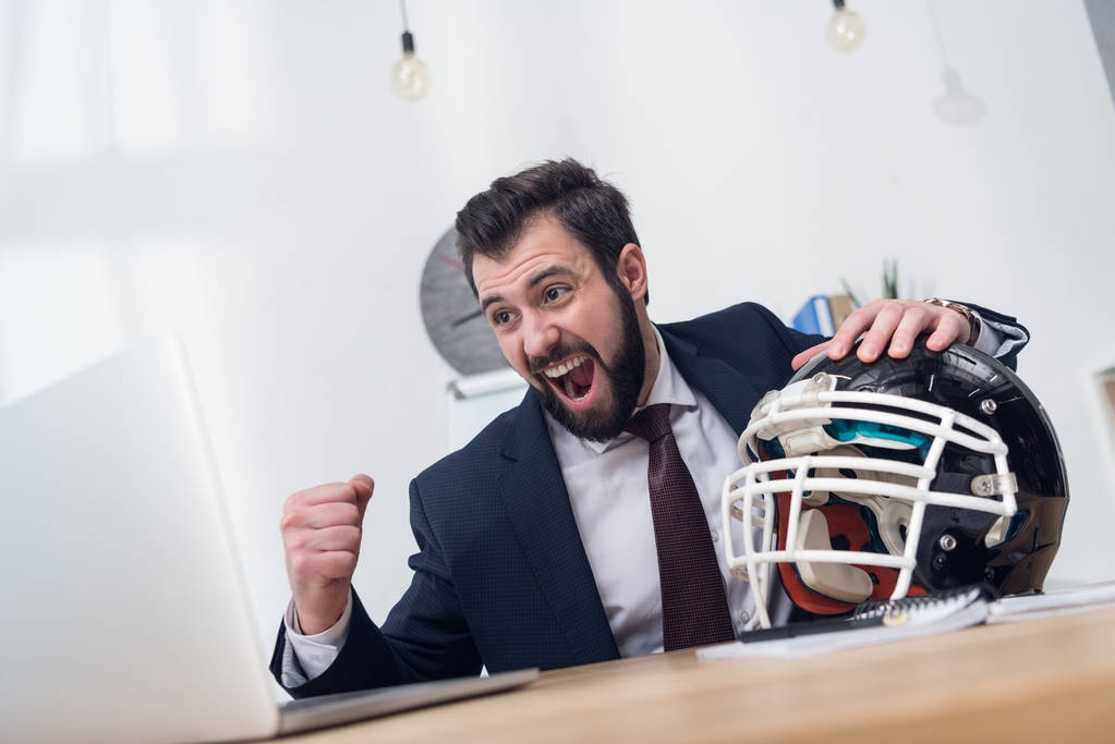 opgewonden zakenman met rugby helm op werkplek op kantoor - Foto, afbeelding