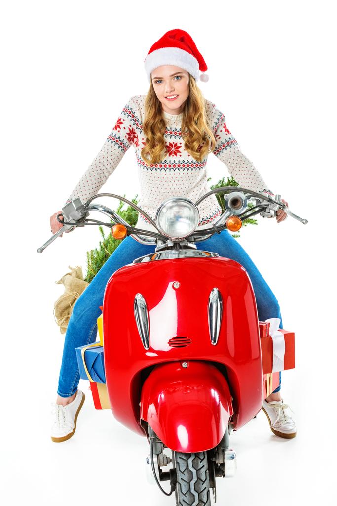 attractive woman in santa hat sitting on red scooter with gifts and christmas tree, isolated on white - Photo, Image