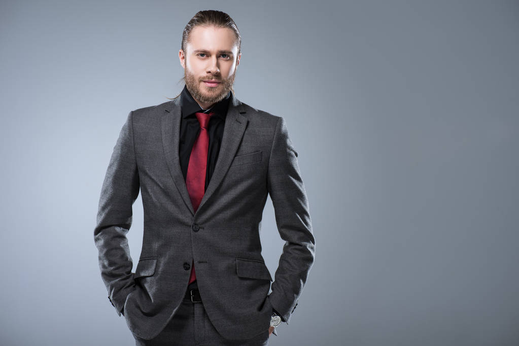 Hombre de negocios en traje formal mirando a la cámara con las manos en el bolsillo, aislado en gris
  - Foto, imagen