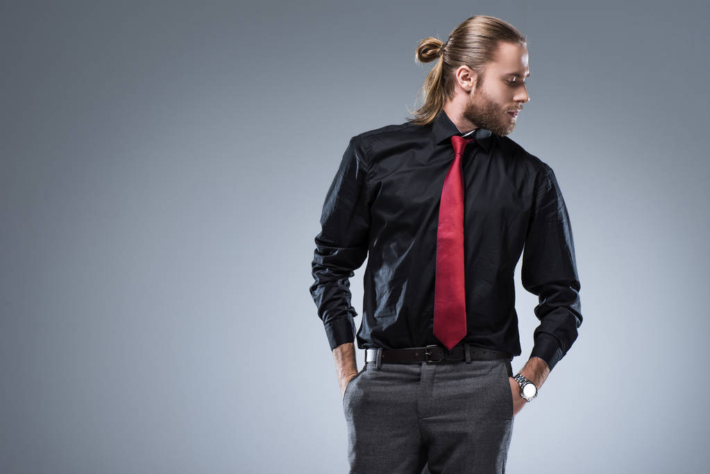 Jovem barbudo homem em camisa preta com gravata vermelha olhando para longe, isolado em cinza
   - Foto, Imagem