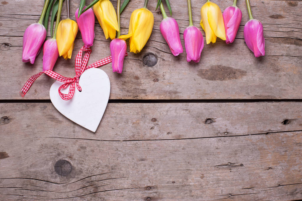 Dekorační srdce bílé a růžové a žluté jarní květiny tulipány na rustikální dřevěné pozadí - Fotografie, Obrázek