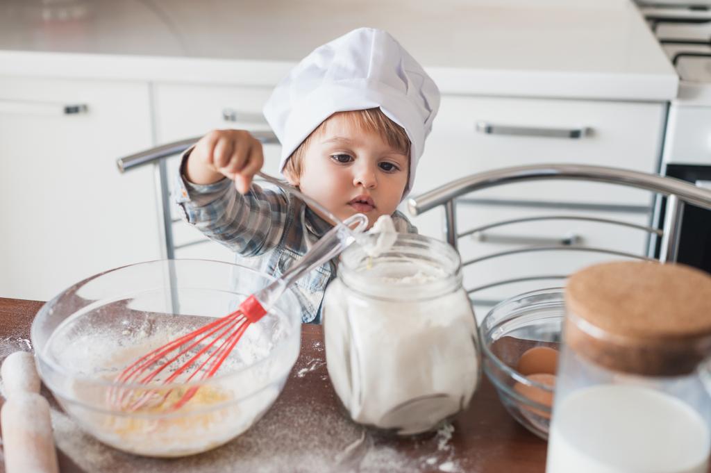pieni lapsi kokki hattu valmistelee taikina keittiössä
 - Valokuva, kuva