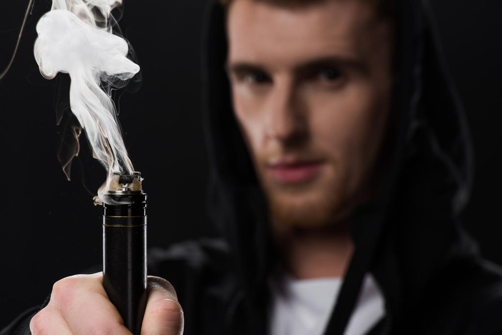 Молодой бородатый человек активирует электронную сигарету, изолированную на черном
 - Фото, изображение