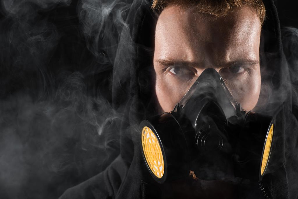 Homem de capuz preto usando máscara protetora de filtro cercado por nuvens de fumaça
 - Foto, Imagem