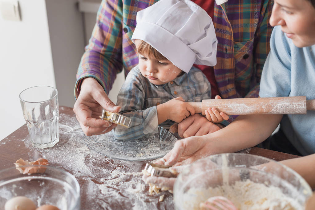 adorable enfant en chapeau de chef préparant la pâte pour les biscuits avec les parents
 - Photo, image